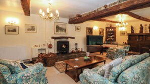 A cozy living room with floral-patterned sofas, a wooden coffee table, a fireplace, and a television. - Stang Farm (Kendal)