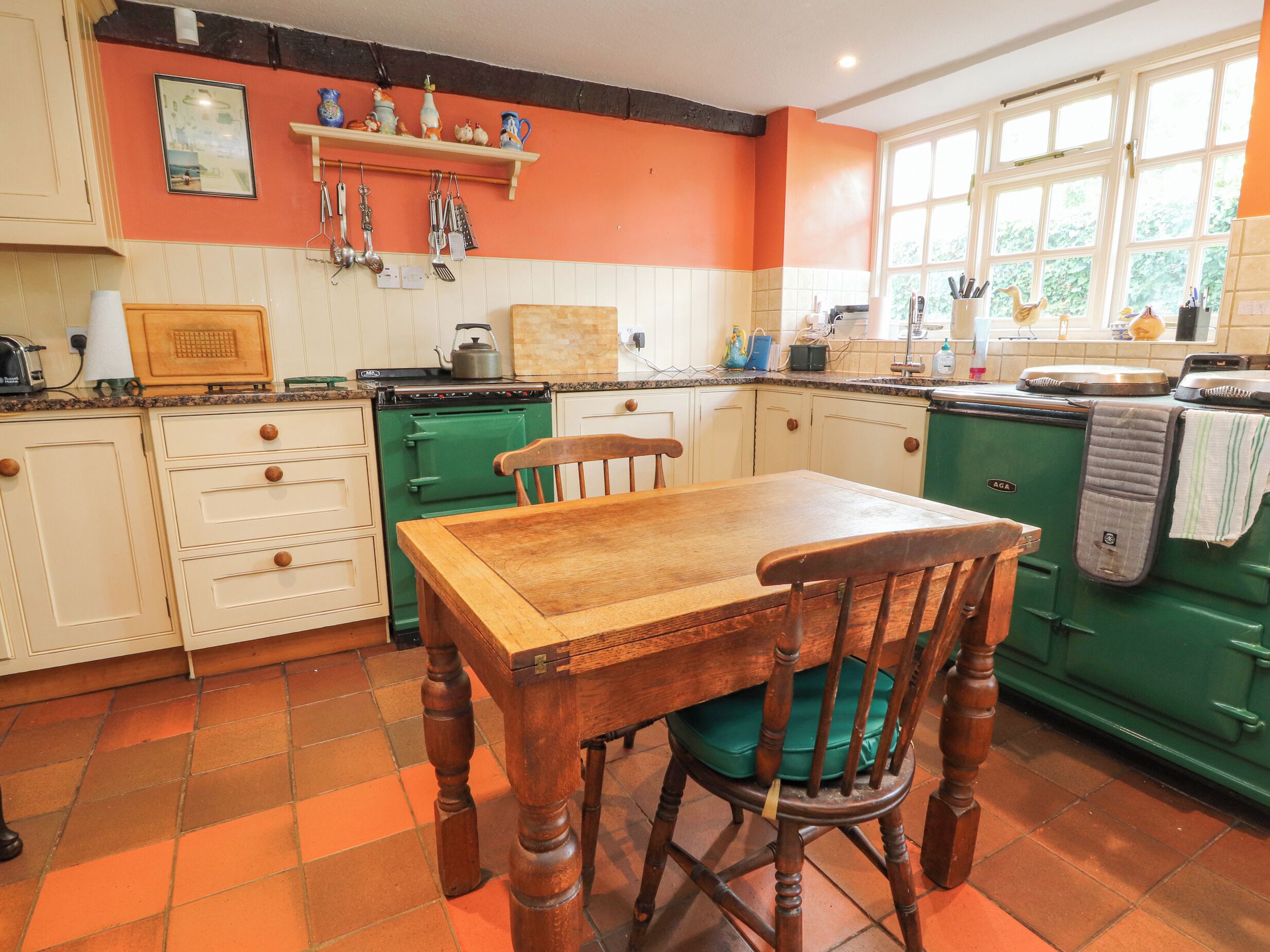 Une cuisine avec des meubles de couleur verte, une table en bois et une chaise. Une fenêtre offre une vue sur la verdure à l’extérieur.