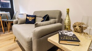 A living room with a grey sofa, two decorative pillows, a book titled 'The Autonomer', a bottle of Prosecco, and a decorative dog head on a wooden table. - Kingfisher Cottage (Canterbury)
