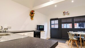 A modern kitchen with a black countertop, white cabinets, and a dining area with a table and chairs. - Kingfisher Cottage (Canterbury)