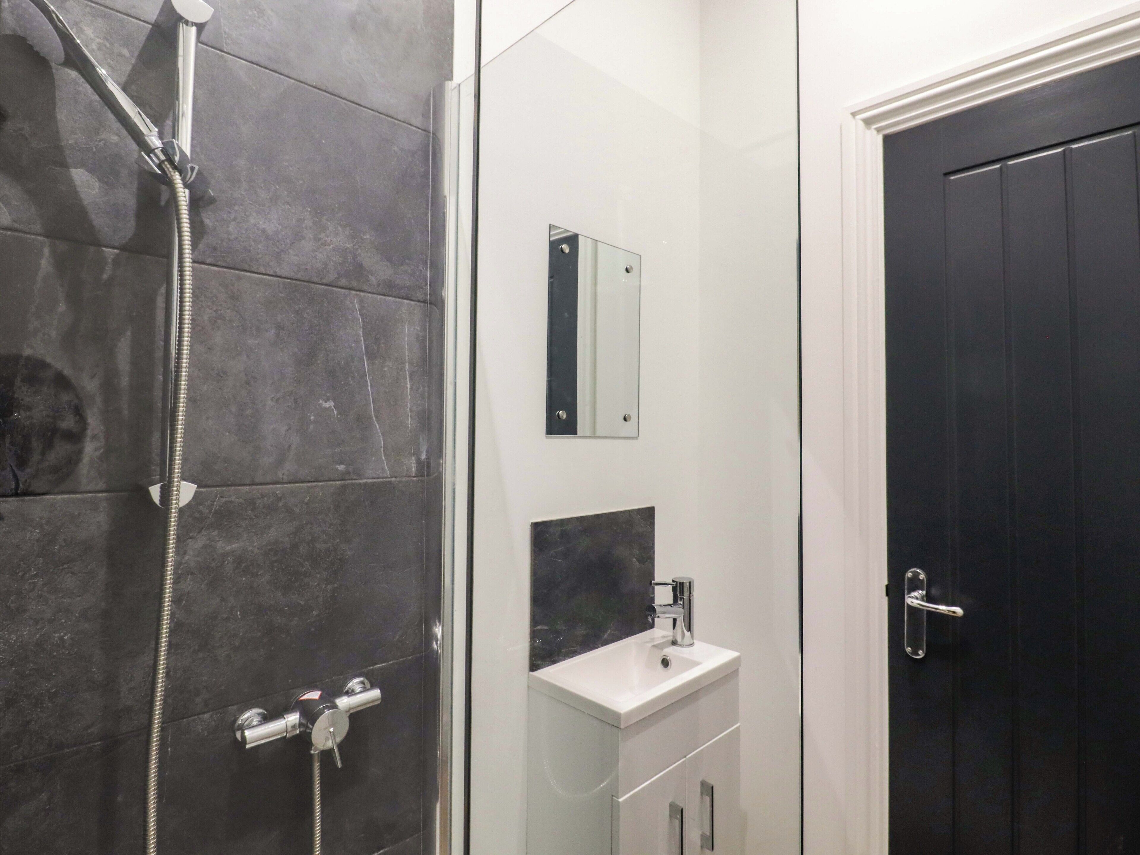 A modern bathroom with a glass shower enclosure, a white sink, and a dark door.