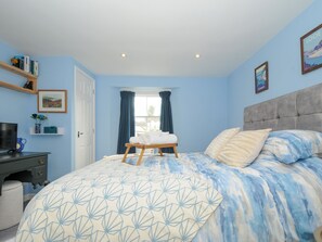Een slaapkamer met een bed, bureau, stoel, raam met gordijnen en een muur met een schilderij.