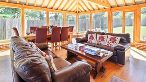 Un patio techado con vigas de madera, un sofá de cuero, una mesa de comedor con sillas y vista a un jardín trasero.