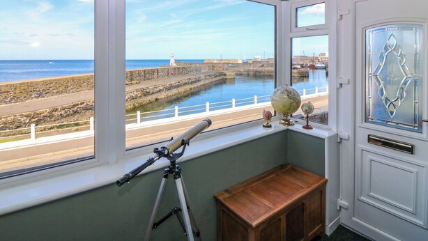 A room with a large bay window overlooking a coastal area, a telescope on a tripod, and a wooden cabinet.