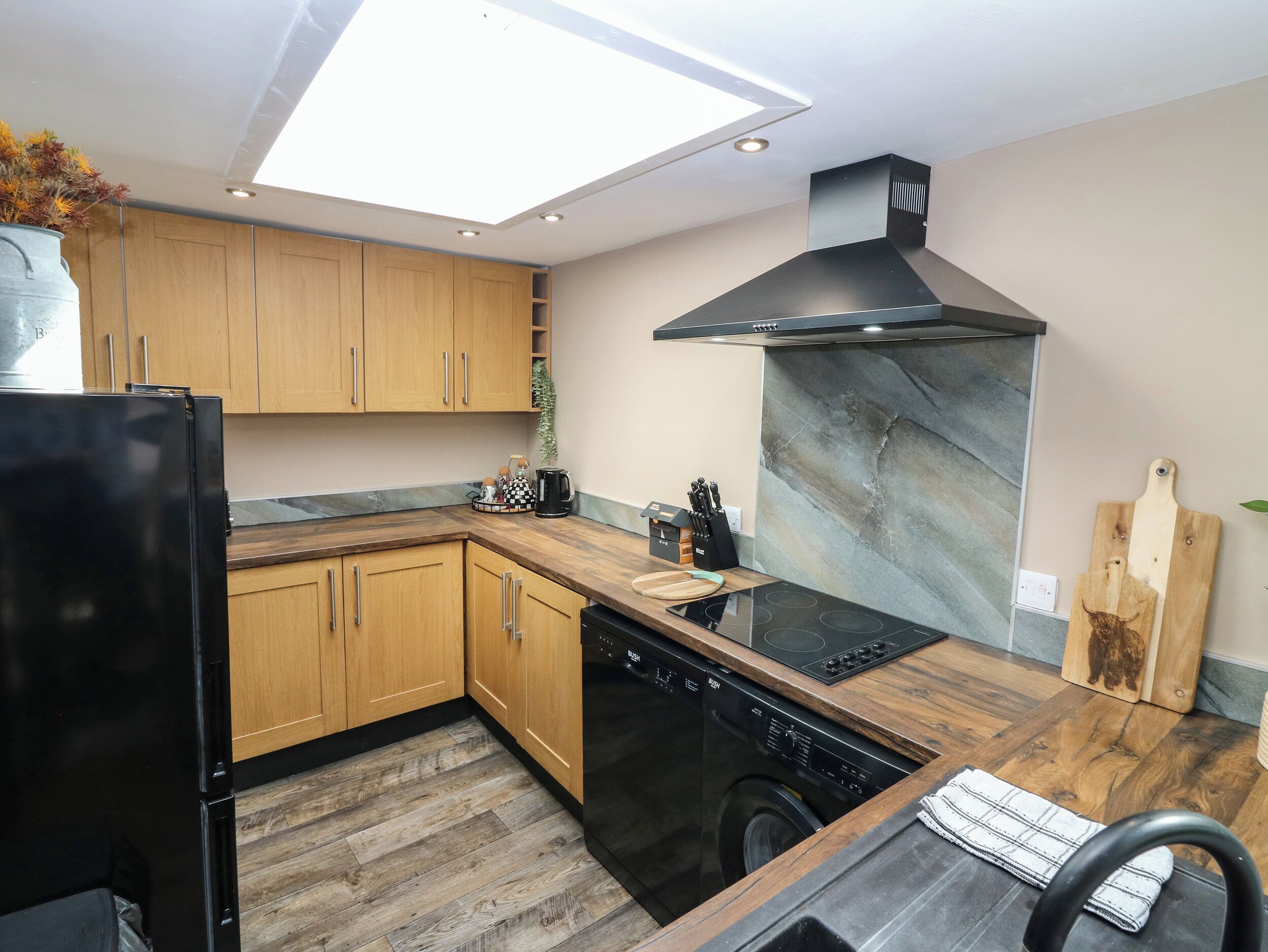 Eine moderne Küche mit Holzschränken, einem schwarzen Kühlschrank, einem Geschirrspüler, einem Induktionskochfeld und einer Marmor-Spritzschutzwand.