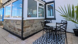 A patio with a table and chairs, a potted plant, and a view of the city through a window.