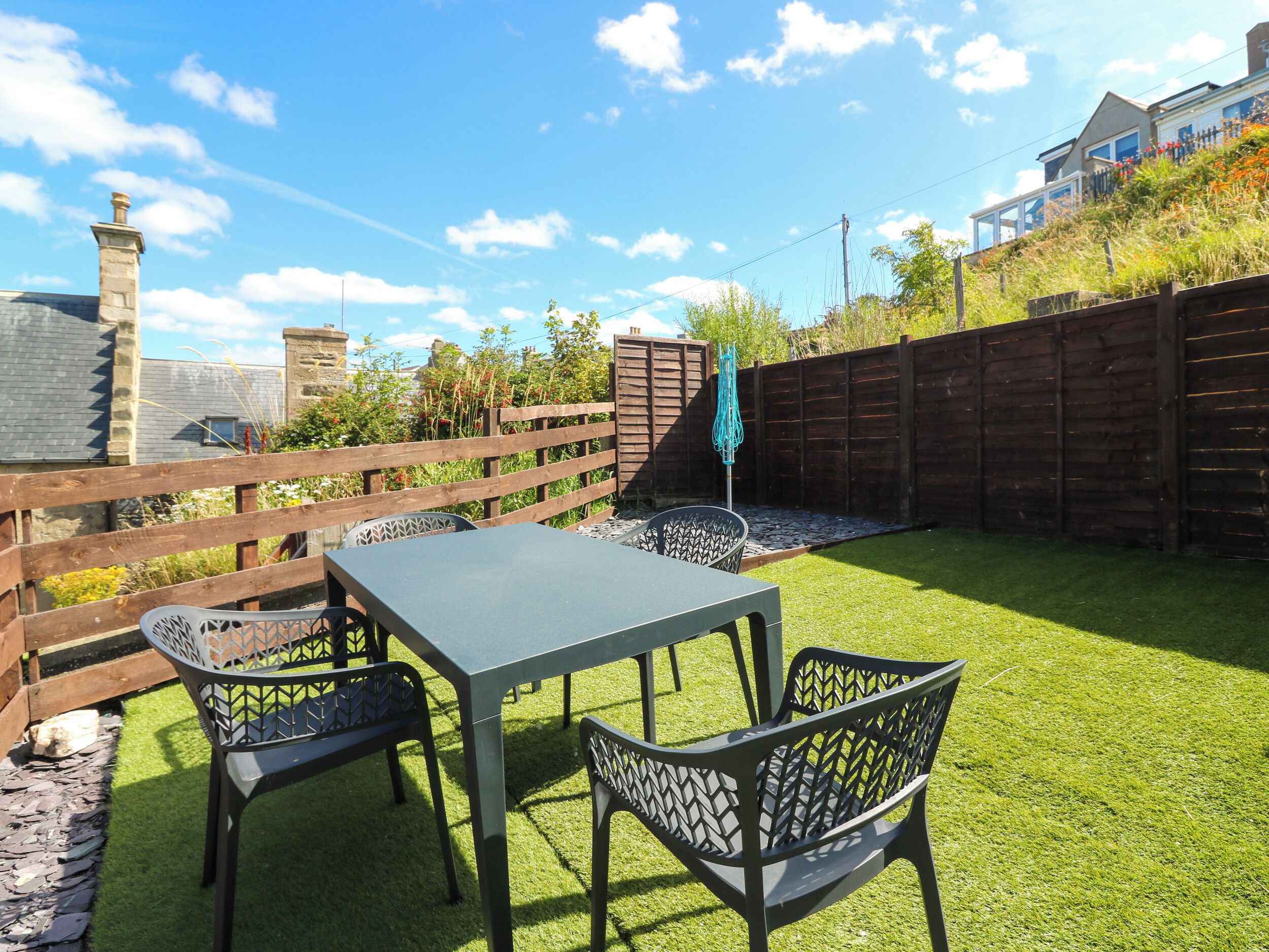 An outdoor patio with a table and chairs, surrounded by a wooden fence and a grassy lawn.