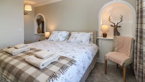 A bedroom with a bed, two bedside lamps, a chair, a deer head decoration, and a mirror.