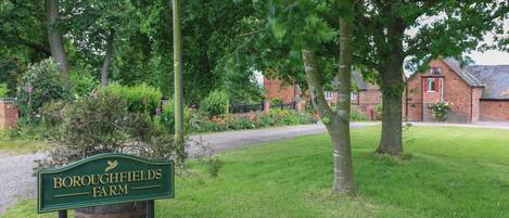A green sign with 'Boroughfields Farm' written on it, surrounded by lush greenery and a brick building in the background.