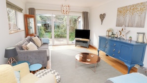 A living room with a grey sofa, a blue cabinet, a TV, and a large window with a view of greenery.