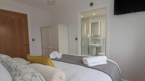 Ett hotellrum med en säng, en garderob, ett badrum med handfat och spegel samt en platt-TV på väggen.