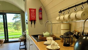 A kitchen with a wooden countertop, a kettle, a teapot, a fire extinguisher, and a window with a view of a green landscape. - Willow (Llanidloes)