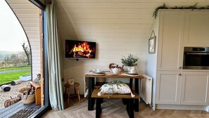 A cozy room with a television displaying a fireplace, a wooden table with a bench, and a kitchen area with cabinets and an oven. - Willow (Llanidloes)