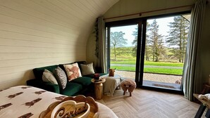 A cozy room with a green sofa, a wooden heart-shaped sign, and a view of a green landscape through large glass doors. - Willow (Llanidloes)