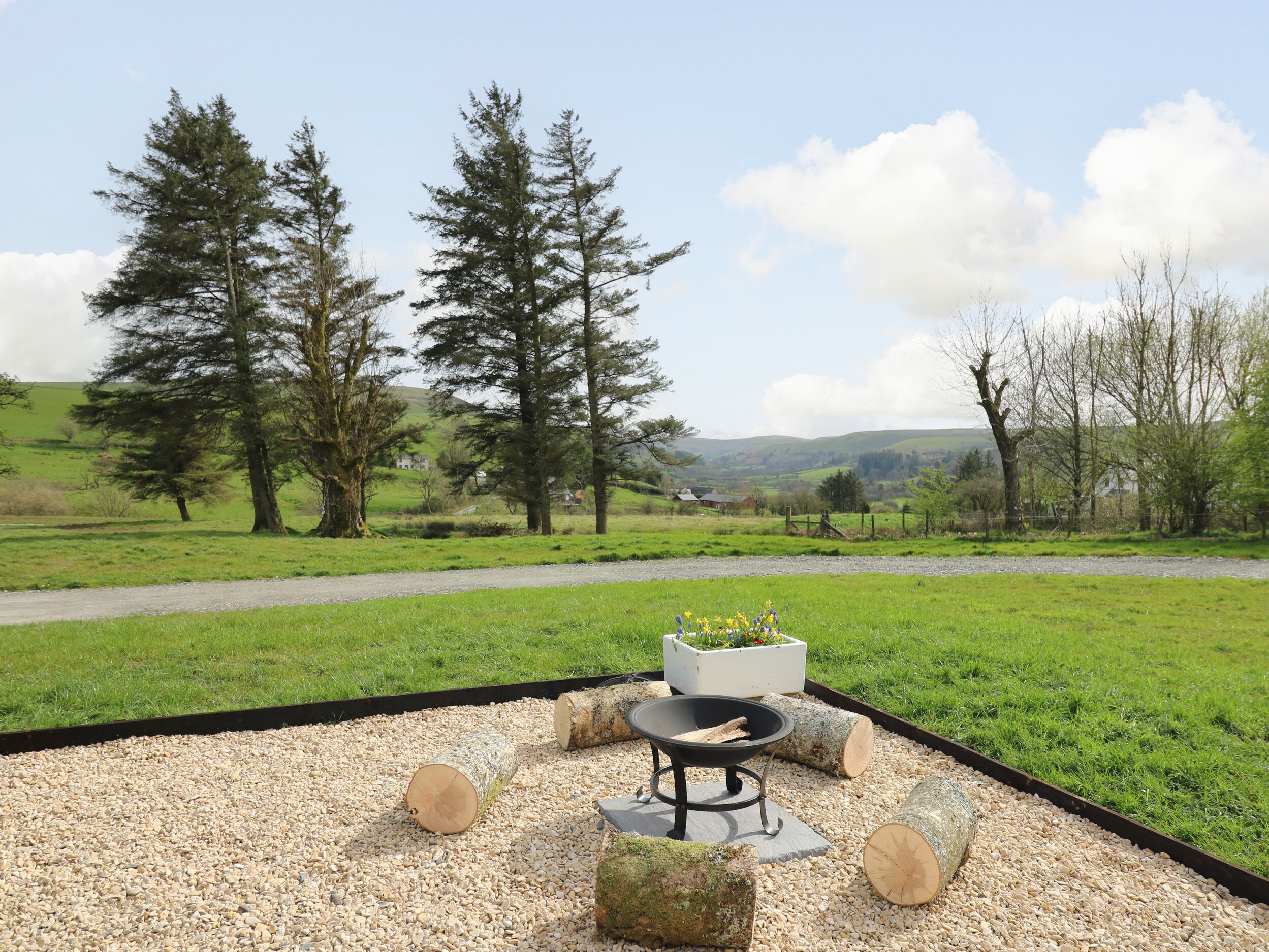 A garden with a fire pit, logs, and a planter with flowers.