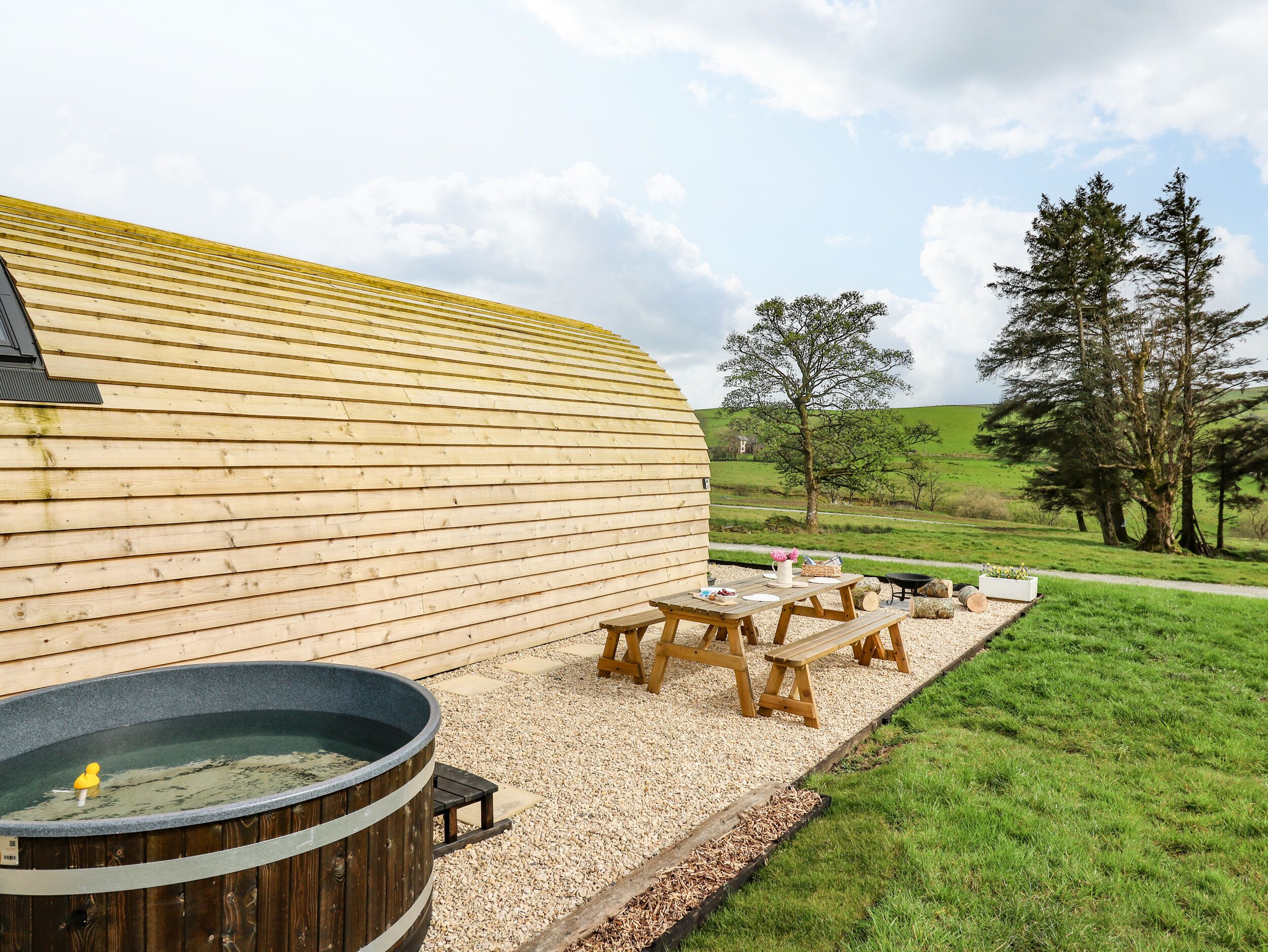 A wooden building with a hot tub, picnic tables, and a gravel patio.