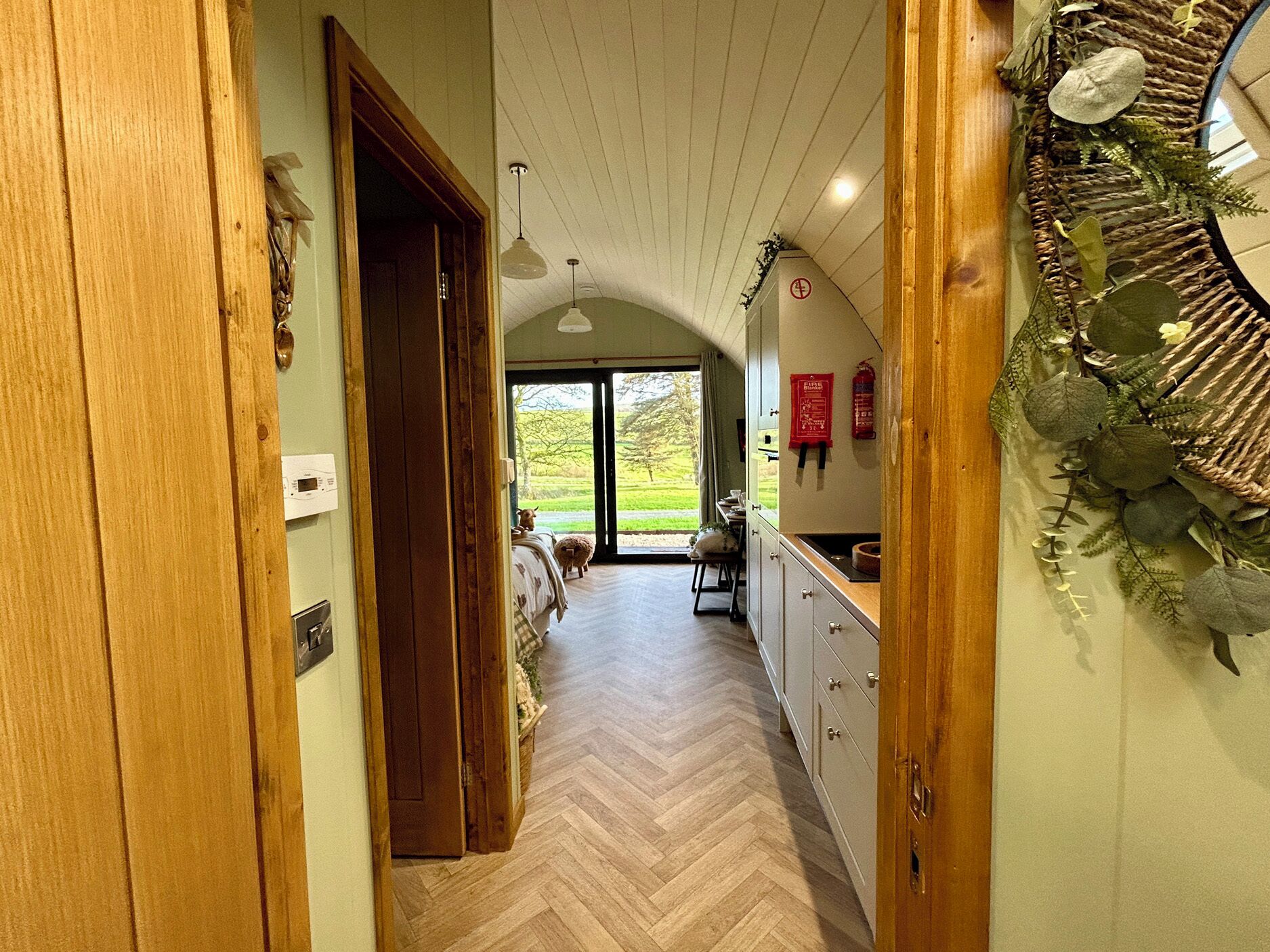 Un couloir doté d’un plancher en bois, d’une porte en bois et offrant une vue sur un paysage verdoyant grâce à une porte vitrée.