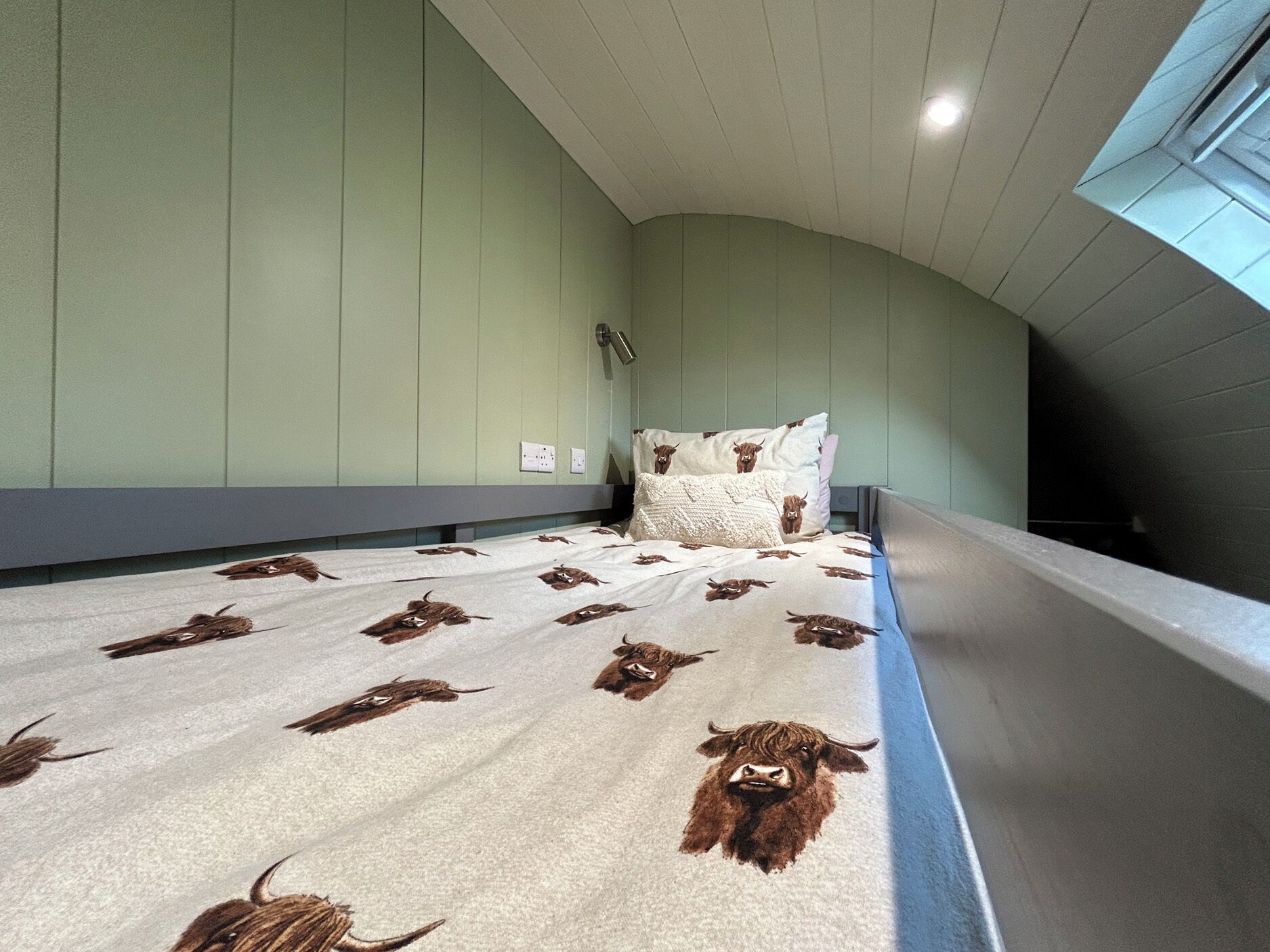 A bedroom with a bed featuring a cow print bedspread, a curved ceiling, and a window on the right side.