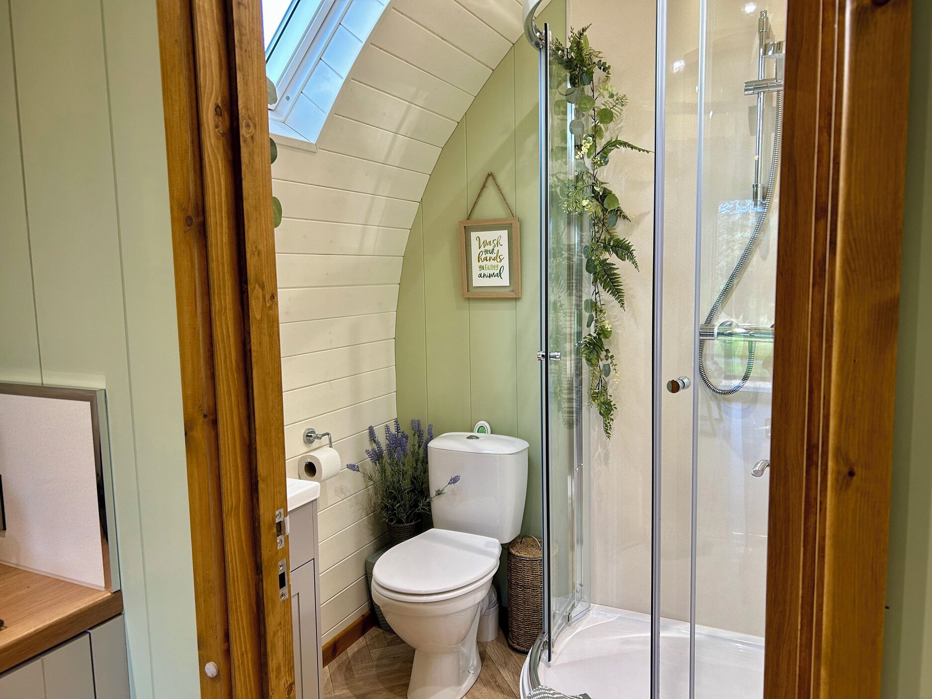 Een badkamer met dakraam, toilet, douche en een klein bordje in een lijst.