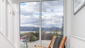 A room with a large sliding glass door leading to a balcony with a view of a lake and mountains.