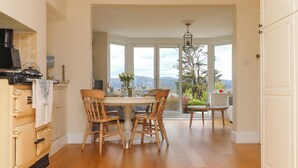 A dining area with a view of mountains, wooden chairs, a table set for two, and a kitchen with a stove.