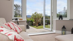 A room with a white sofa, a small table, and a view of a garden through large sliding glass doors.