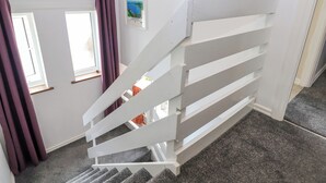 Eine weiße Treppe mit Geländer, die zu einer Zwischenebene mit Tür und Fenstern führt.
