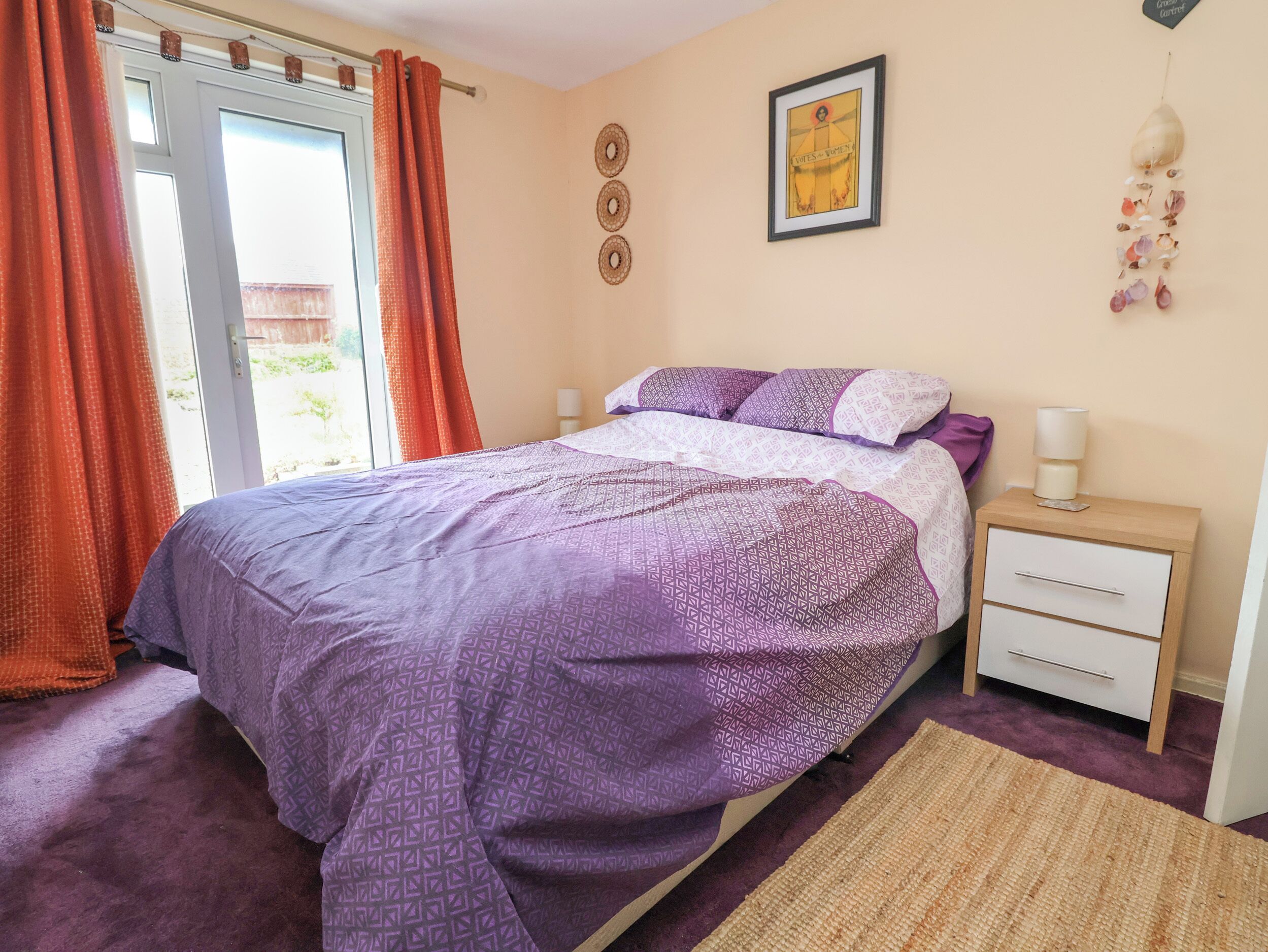 A bedroom with a bed, a nightstand, a wall-mounted picture, and a window with curtains.