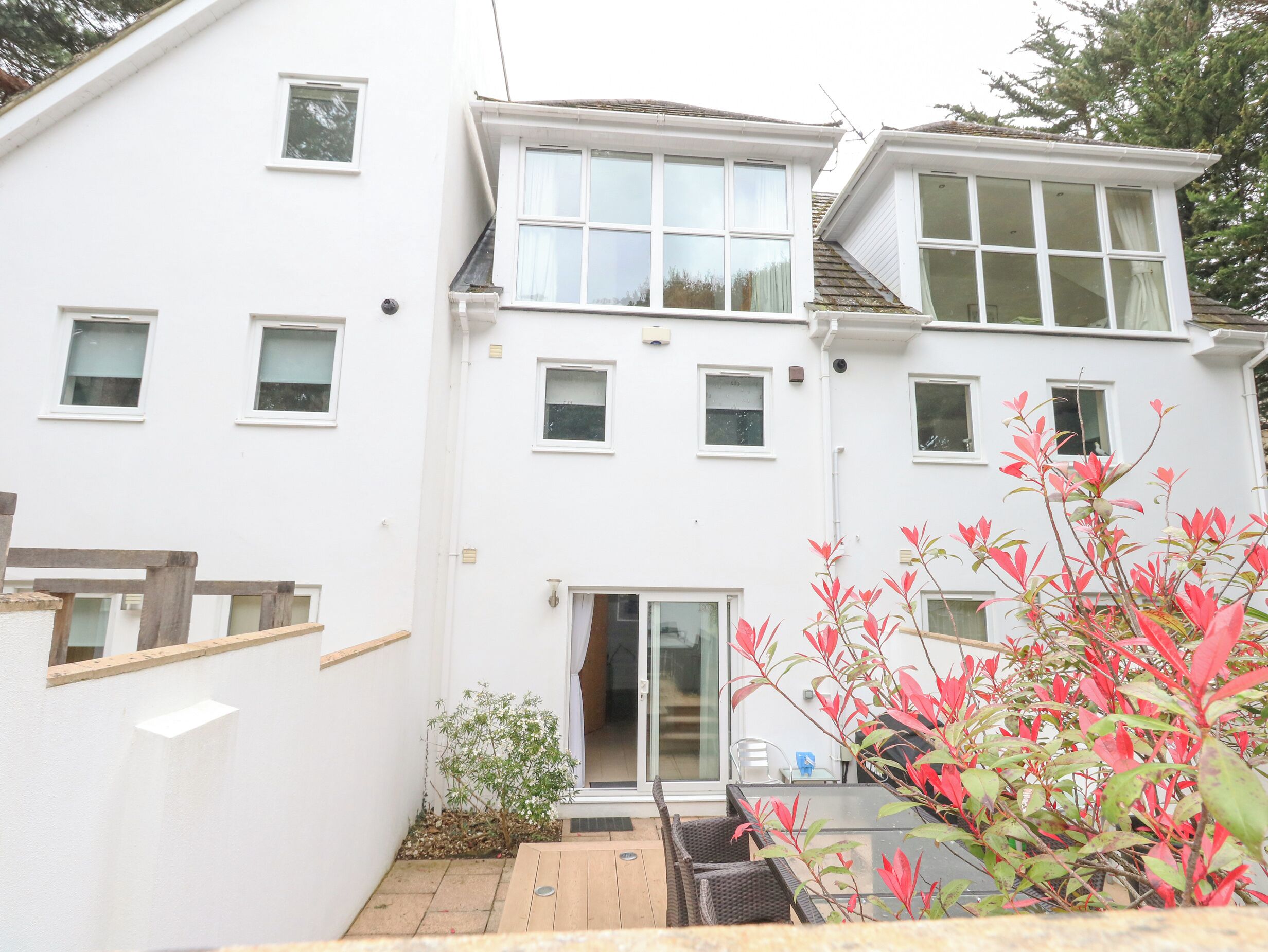 A two-story residential building with multiple windows, a sliding glass door, and a small garden area with a table and chairs.