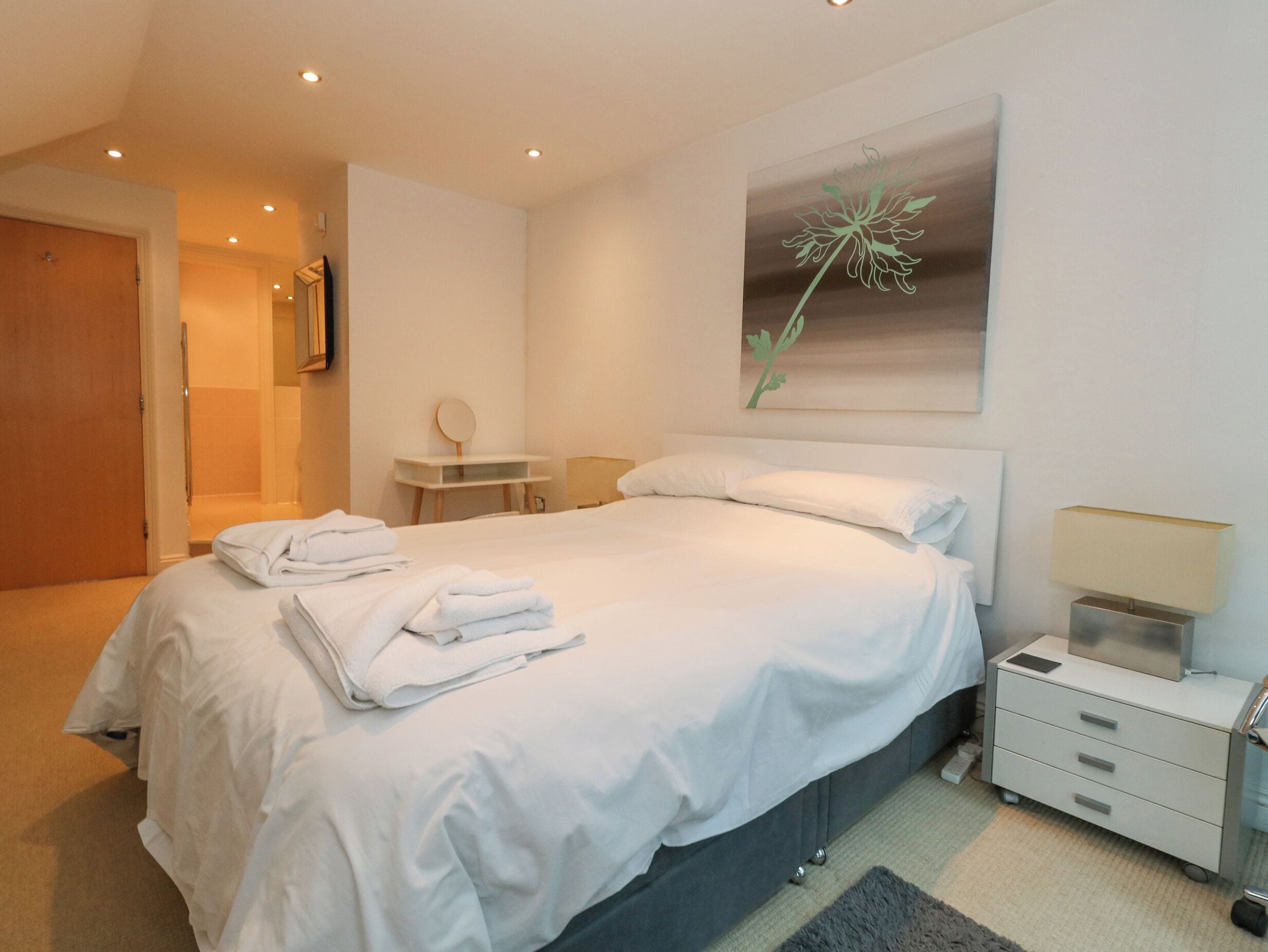 A neatly made bed with folded towels, a bedside table with a lamp, and a wall-mounted artwork.