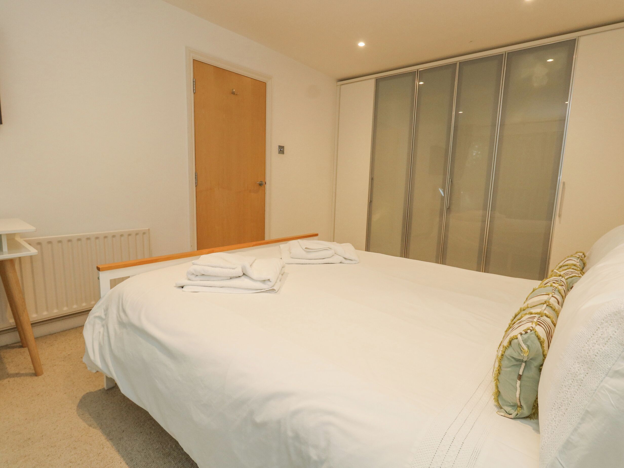 A neatly made bed with white linens and a folded towel on the side.
