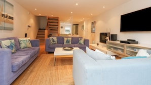 A modern living room with two sofas, a coffee table, a TV, and a staircase leading to an upper level. - 5 Red Sails (Poole)