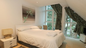 A bedroom with a bed, a nightstand, a lamp, a dresser, a window with curtains, and a painting on the wall. - 5 Red Sails (Poole)