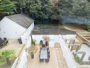 A patio with a table and chairs, a small garden area with potted plants, and a view of a pond. - 5 Red Sails (Poole)