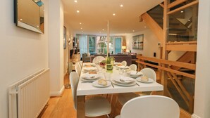 A dining area with a long table set for four, surrounded by chairs, with a staircase and a large window in the background. - 5 Red Sails (Poole)
