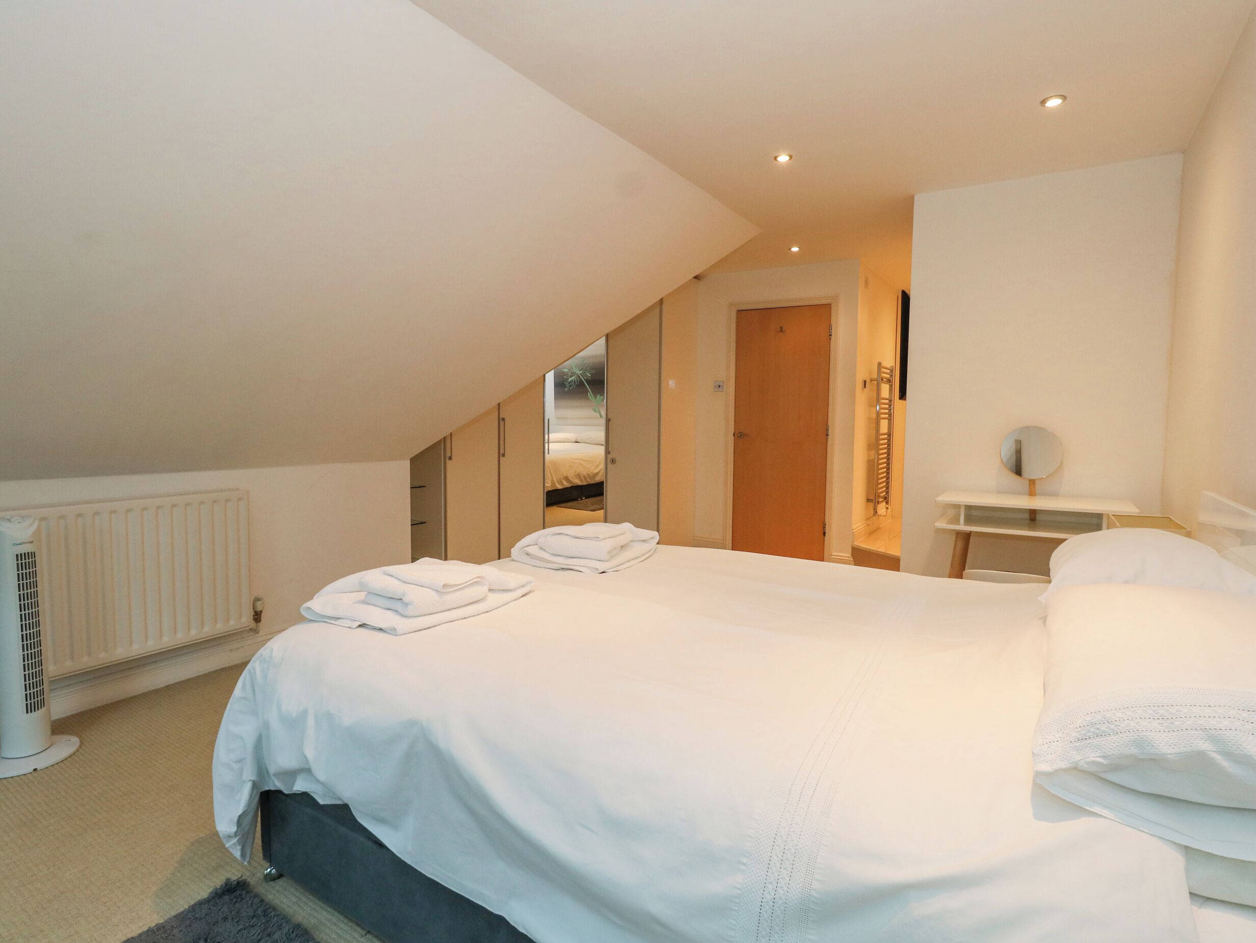 A bedroom with a large bed, a radiator, a mirror, and a door leading to another room.