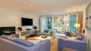 A modern living room with a large flat-screen TV, two sofas, a coffee table, and a dining area with a table and chairs. - 5 Red Sails (Poole)