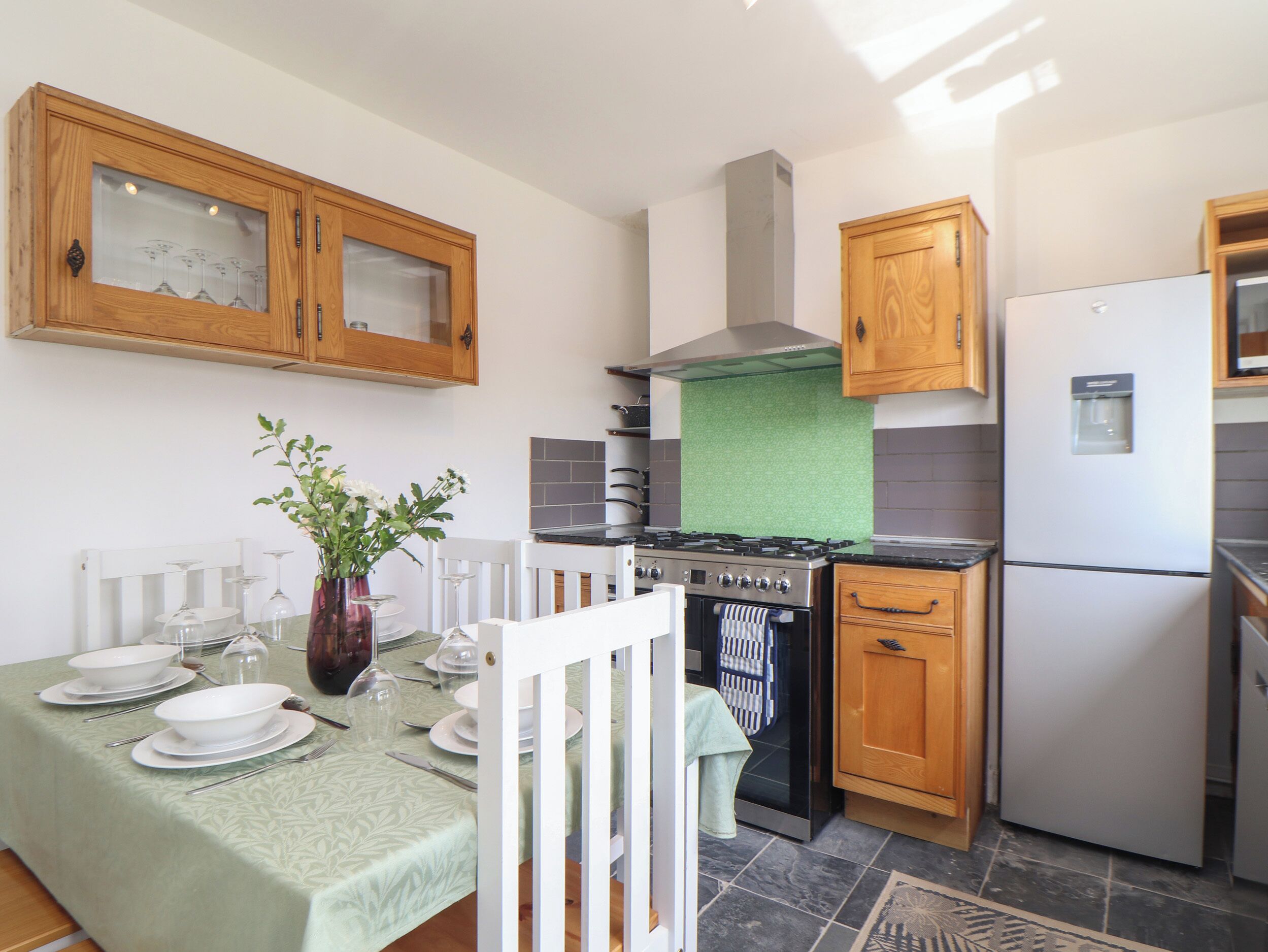 A kitchen with wooden cabinets, a stove, a refrigerator, and a dining table set for four.