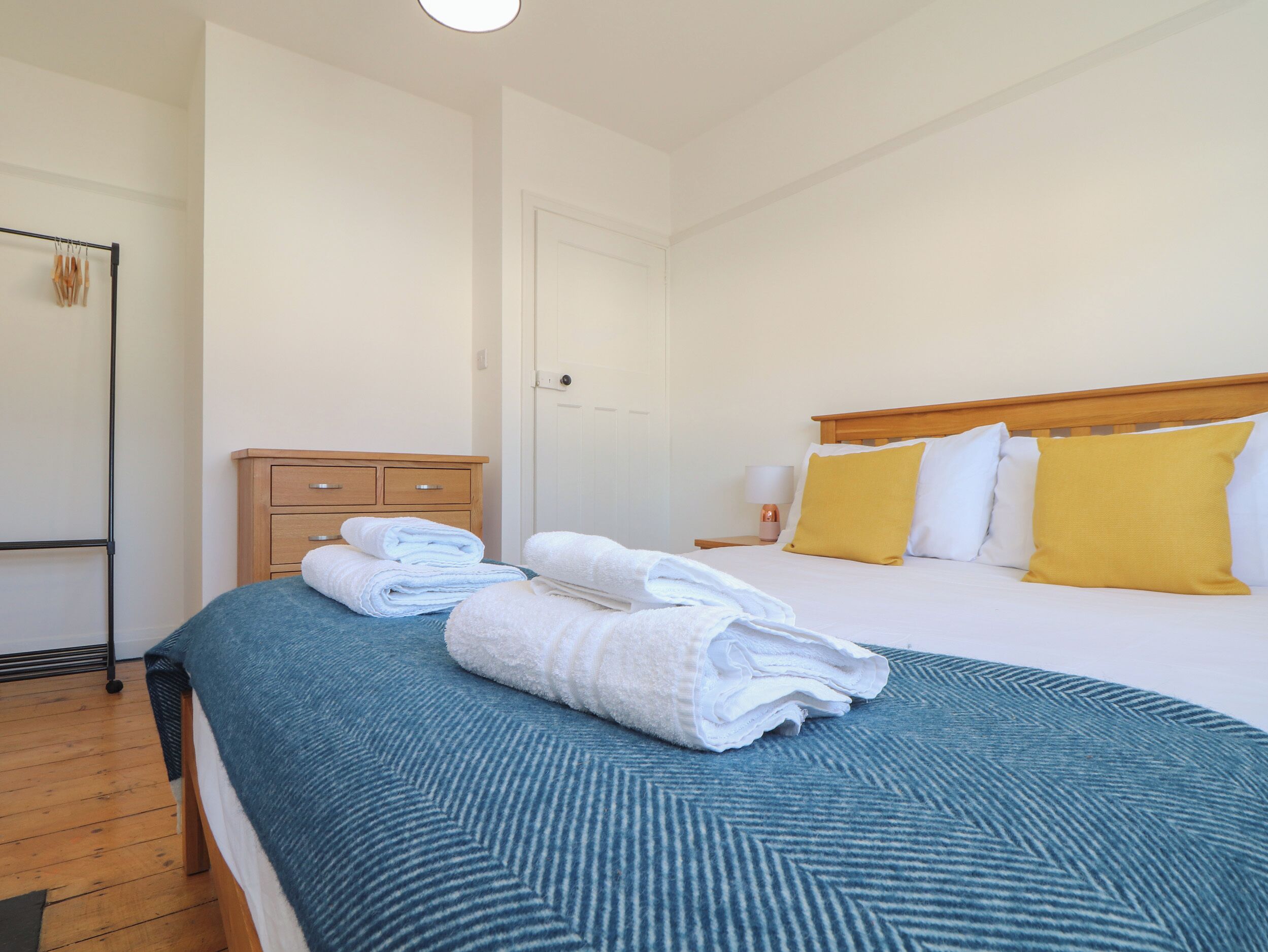 A neatly made bed with a blue and white striped bedspread, two white towels, and two yellow pillows.