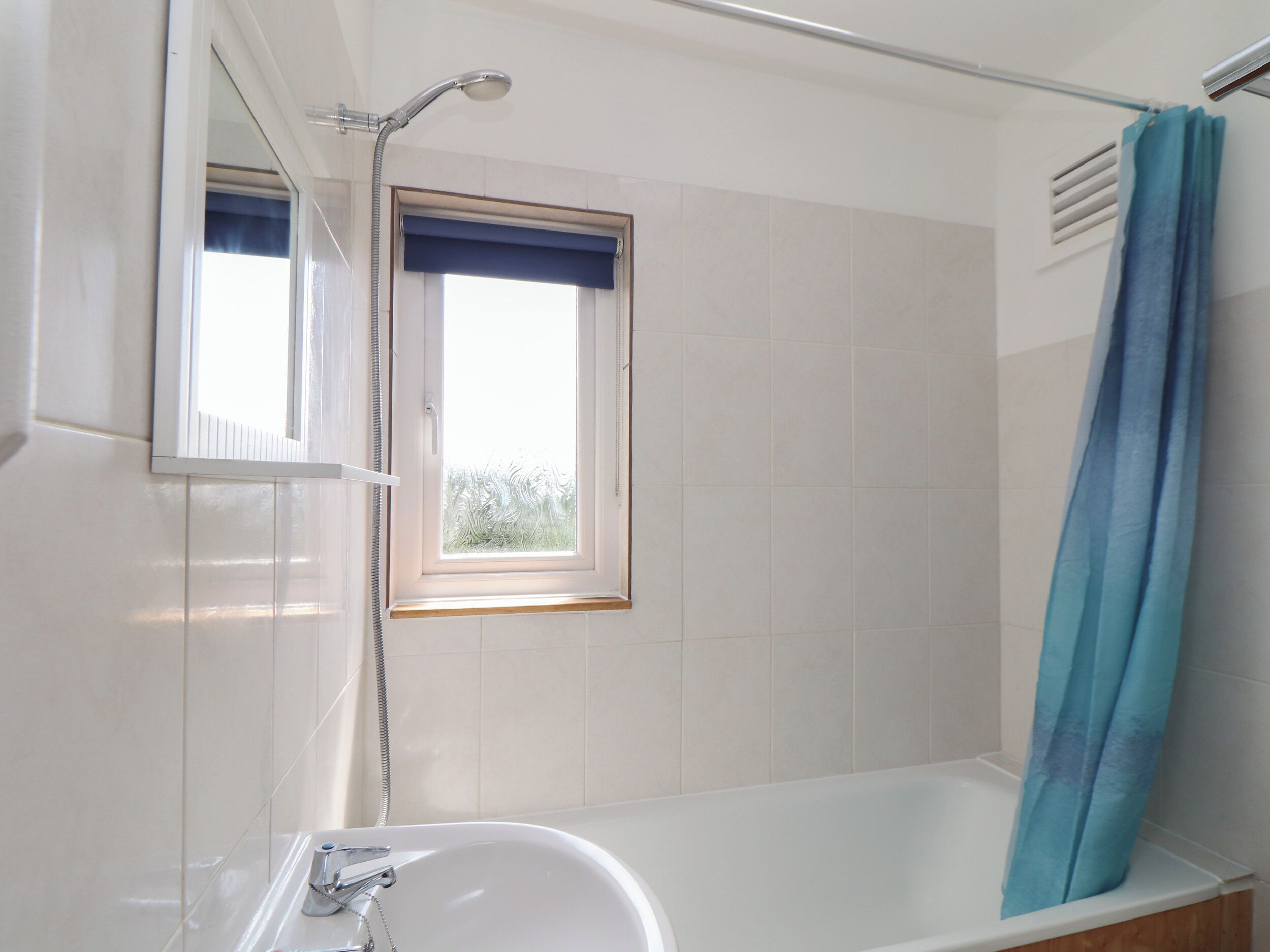 Une salle de bain avec une baignoire, une douche et une fenêtre ornée d’un rideau bleu.