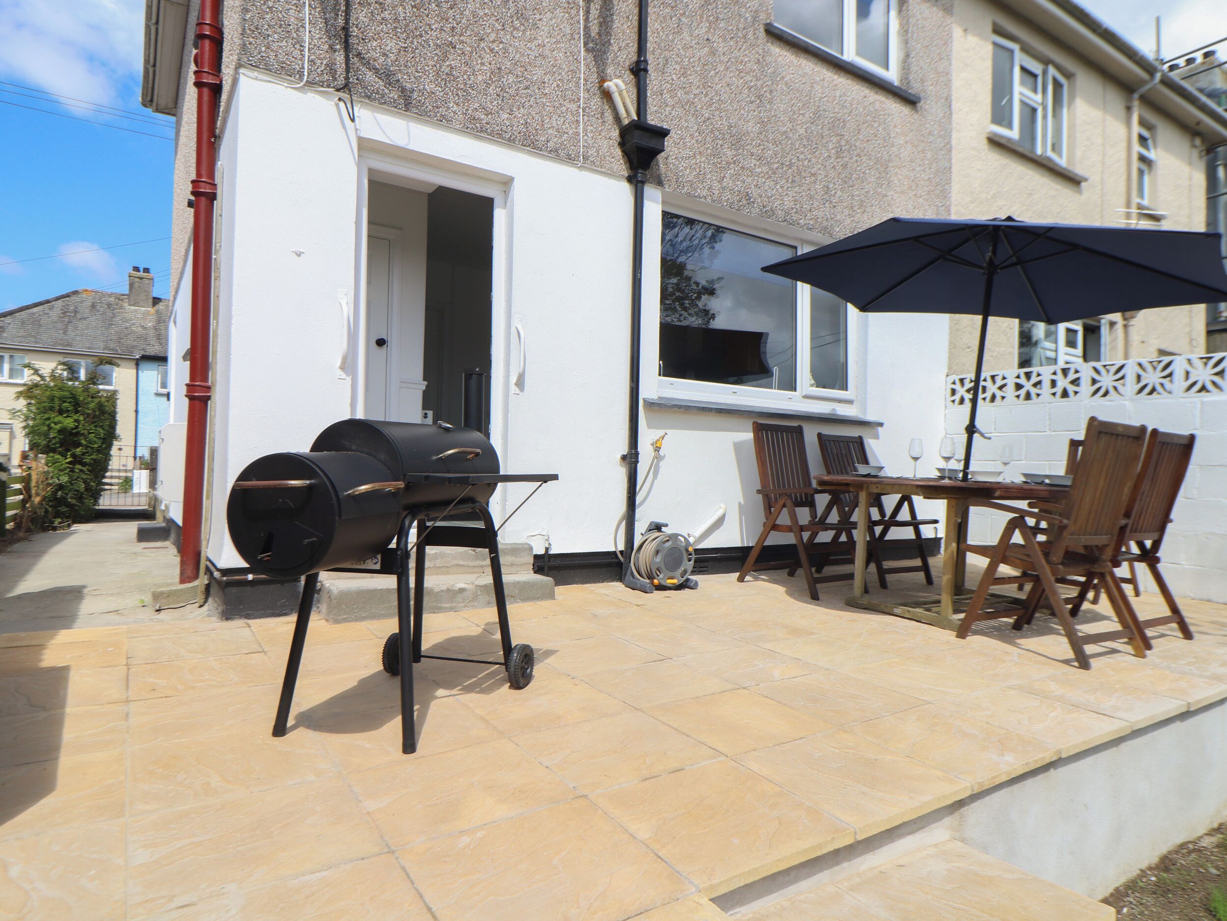 An outdoor patio with a barbecue grill, a table with chairs, and an umbrella.