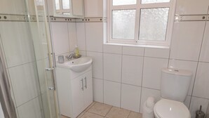 A bathroom with a glass shower enclosure, a sink with a mirror above it, a toilet, and a window. - 2 Carlton Cottage (Enniskillen)