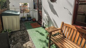 Ein kleiner Patio-Bereich mit einer hölzernen Bank, Pflanzkübeln und einem Tisch.
