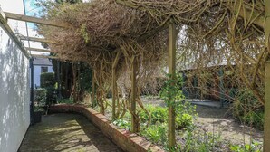 Ein gepflasterter Weg führt zu einem überdachten Gartenbereich mit einer Pergola.