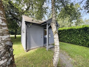 A small, single-story building with a dark exterior, a door, and a small porch area. - Maple (Winkleigh)