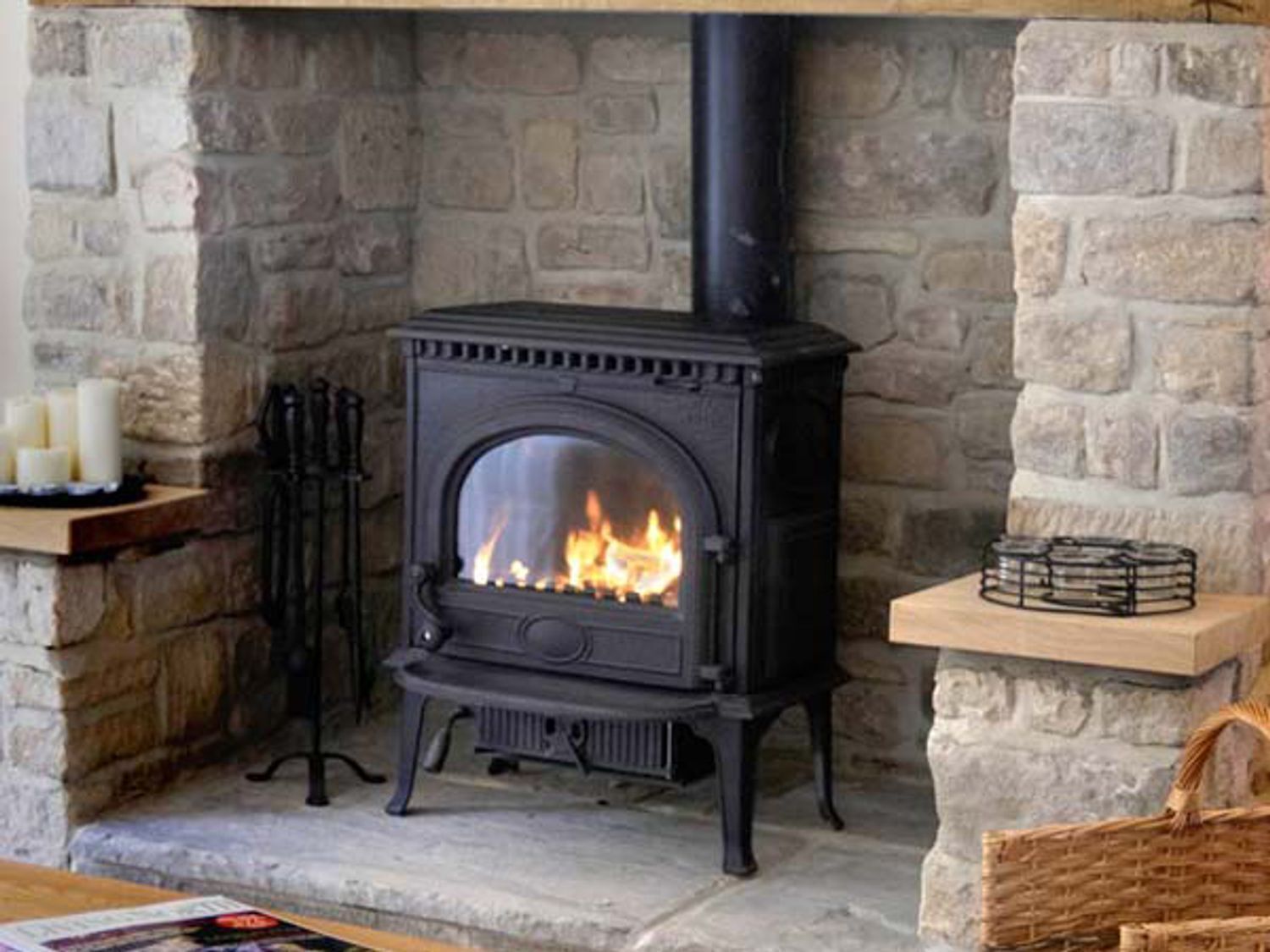 A stone fireplace with a black wood-burning stove, a candle holder, and a basket on the mantel.