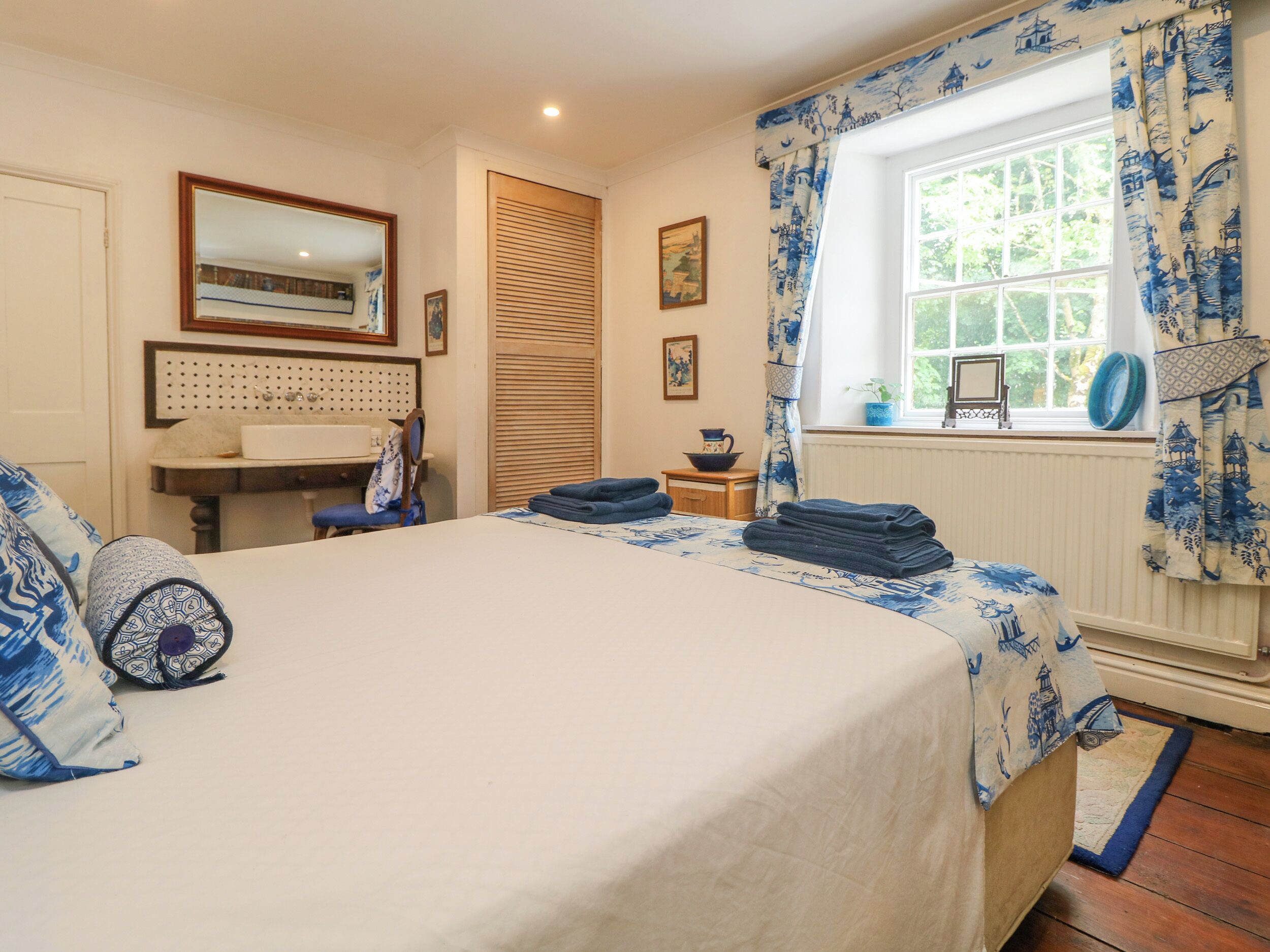 A bedroom with a bed, a desk, a chair, a window with curtains, and a radiator.