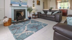A living room with a fireplace, a sofa, a coffee table, and a rug. - Connie's Cottage (Helston)
