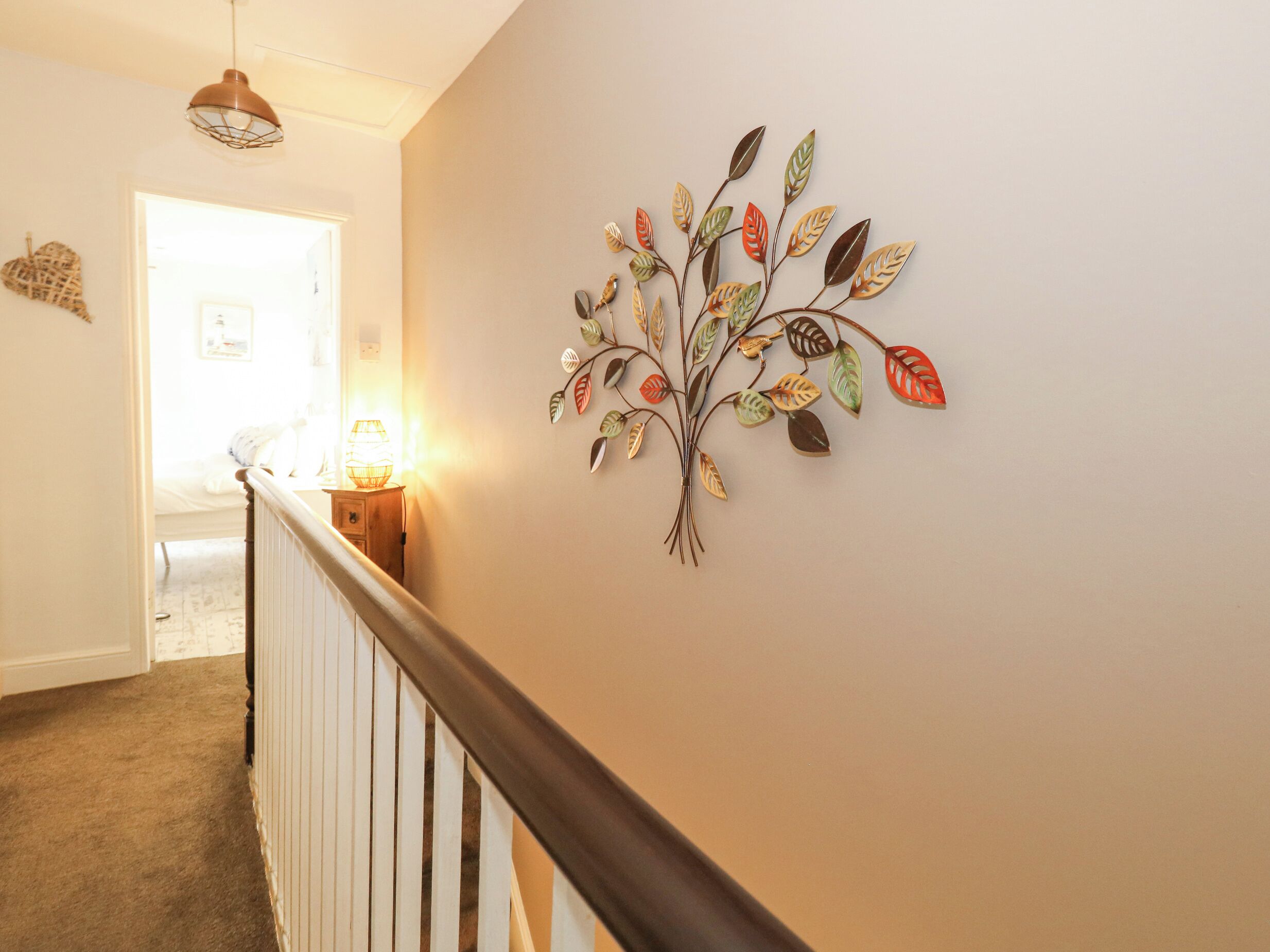 A hallway with a wooden railing, a wall-mounted decorative leaf art piece, and a doorway leading to another room.