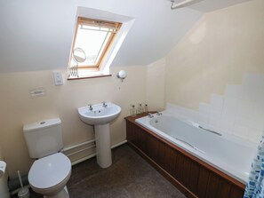 A bathroom with a skylight, a sink, a toilet, and a bathtub.